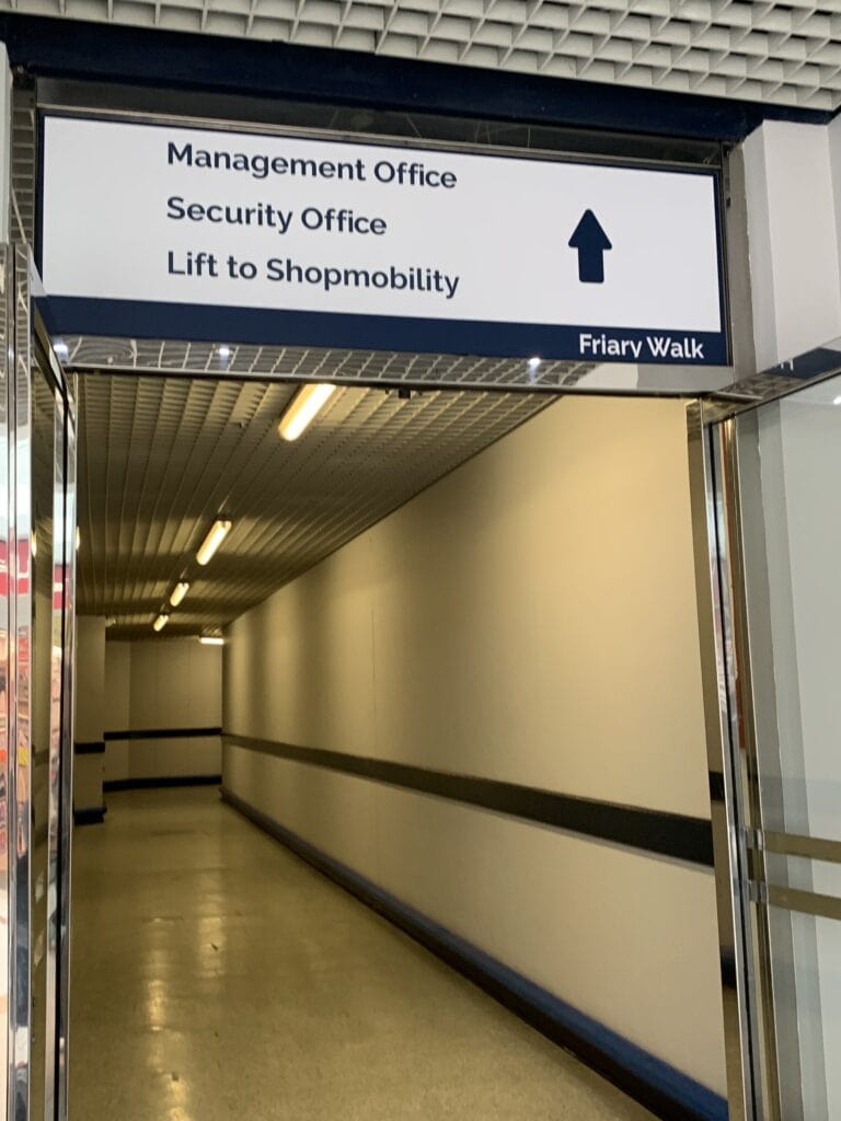 Passageway in Friary Walk with overhead sign directing to the lift to ShopMobility Worcester.